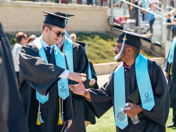 Two UIU graduates shake hands at commencement